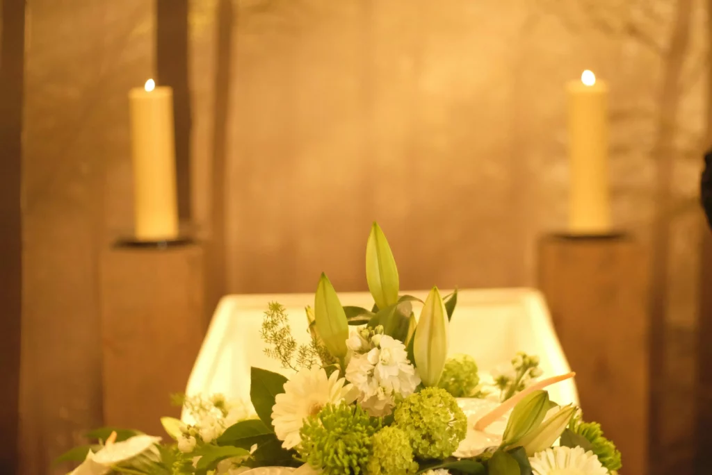 Composition florale avec lys blancs et bougies près d'un cercueil lors d'obsèques.