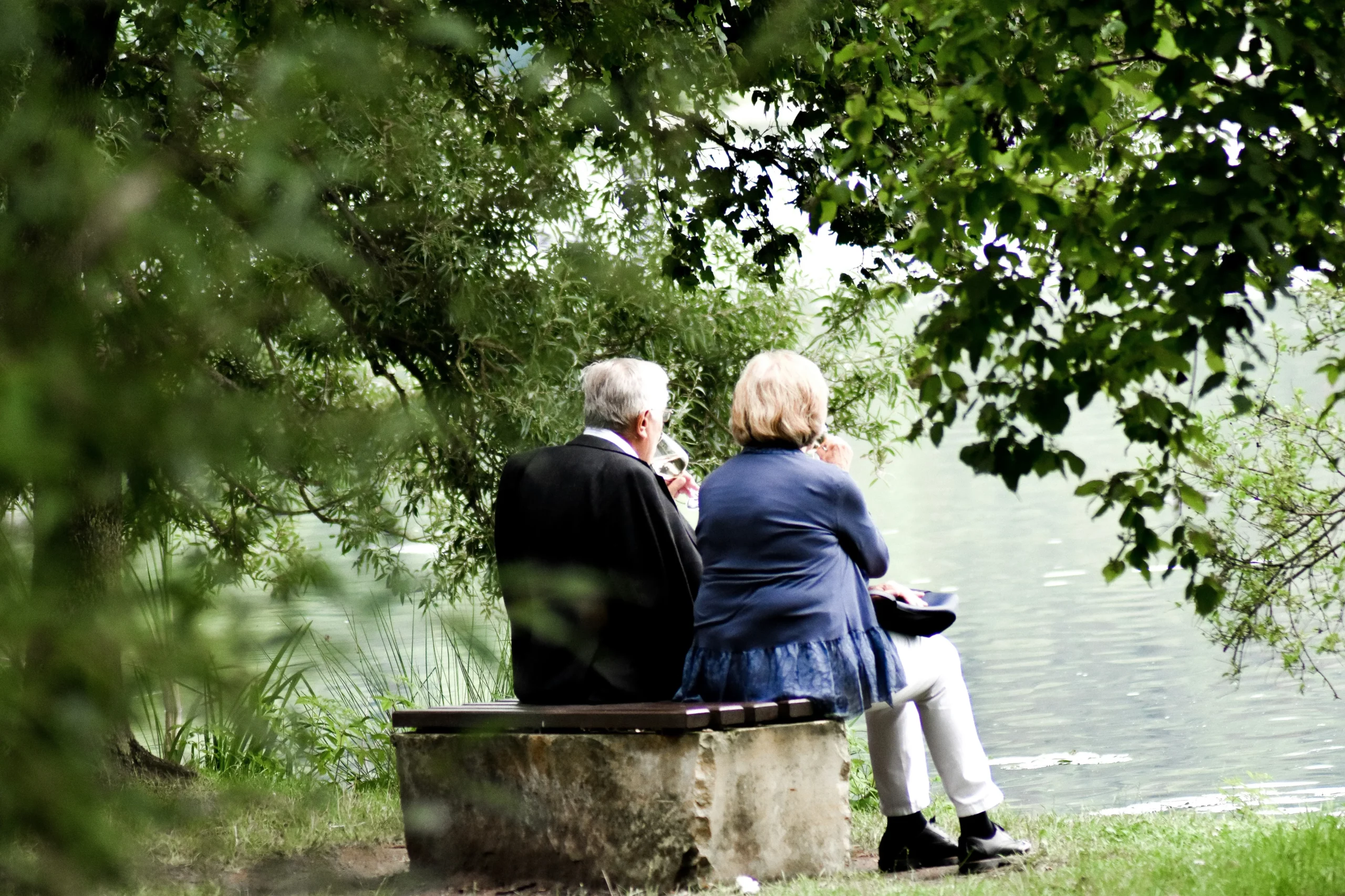 Couple de seniors assis sur un banc en pleine nature au bord de l'eau.
