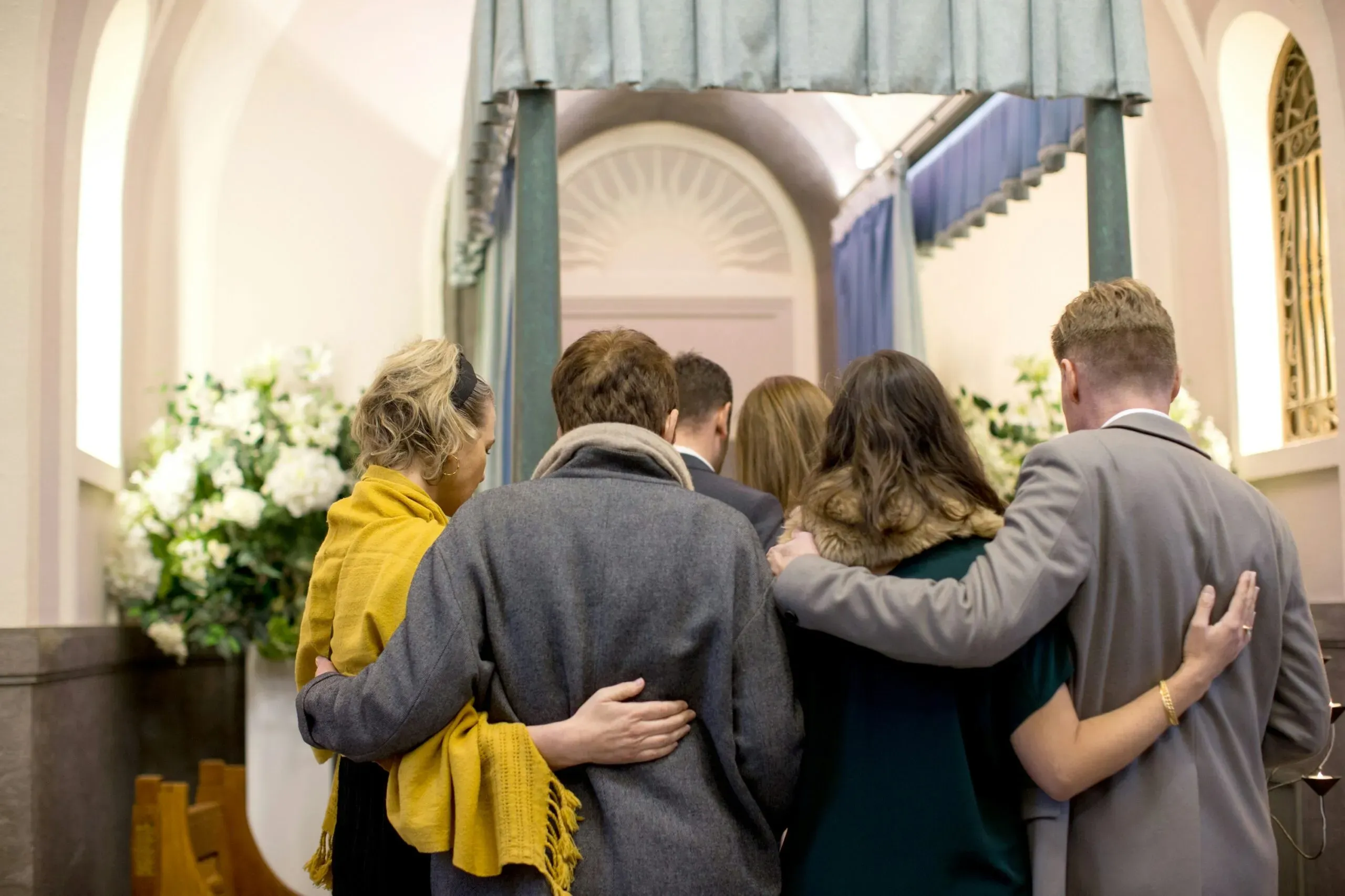 Proches en deuil se soutenant lors d'une cérémonie d'adieu dans un funérarium.